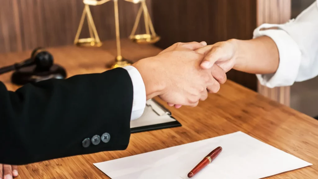 A lawyer and a client shakes hands over what seems to be the lawyer’s office table.