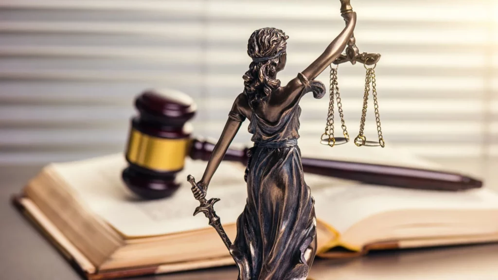 Lady Justice is in the foreground while a gavel over an open law book is in the blurred background. 