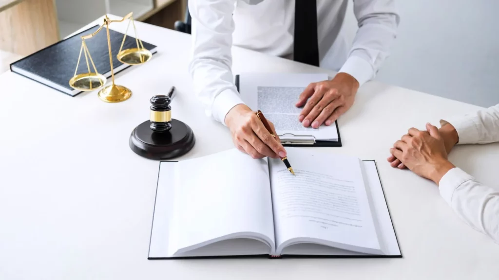 A lawyer’s arm is seen signing on the pages of a legal document. 